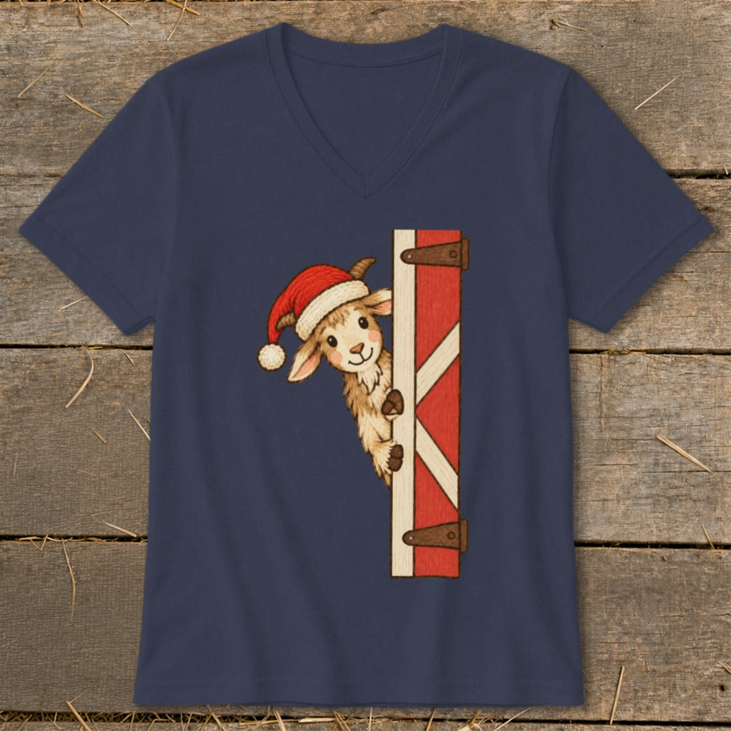 Goat wearing Santa hat peeks around a red barn door on navy t-shirt.