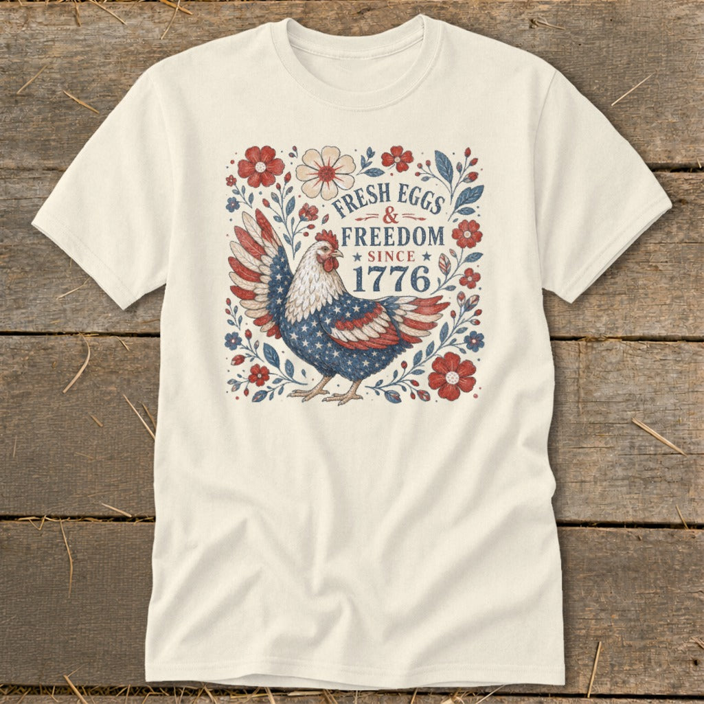 Cream t-shirt with patriotic chicken graphic and text "FRESH EGGS & FREEDOM SINCE 1776".