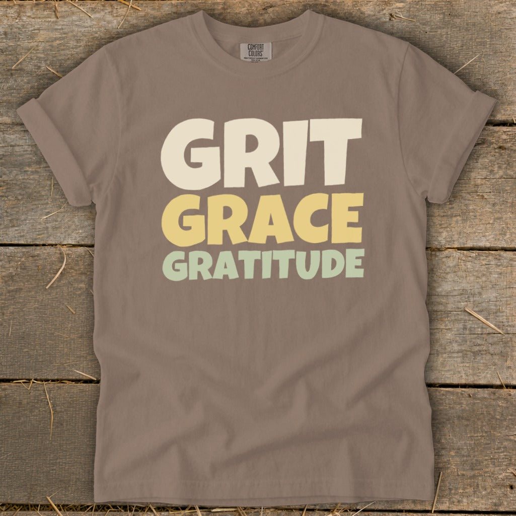 Brown t-shirt featuring the stacked text Grit, Grace, Gratitude in cream, yellow, and green.