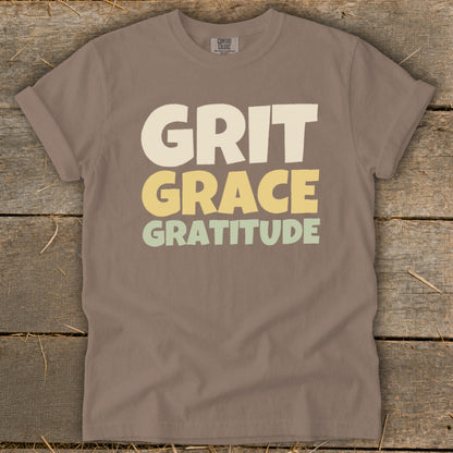 Brown t-shirt featuring the stacked text Grit, Grace, Gratitude in cream, yellow, and green.