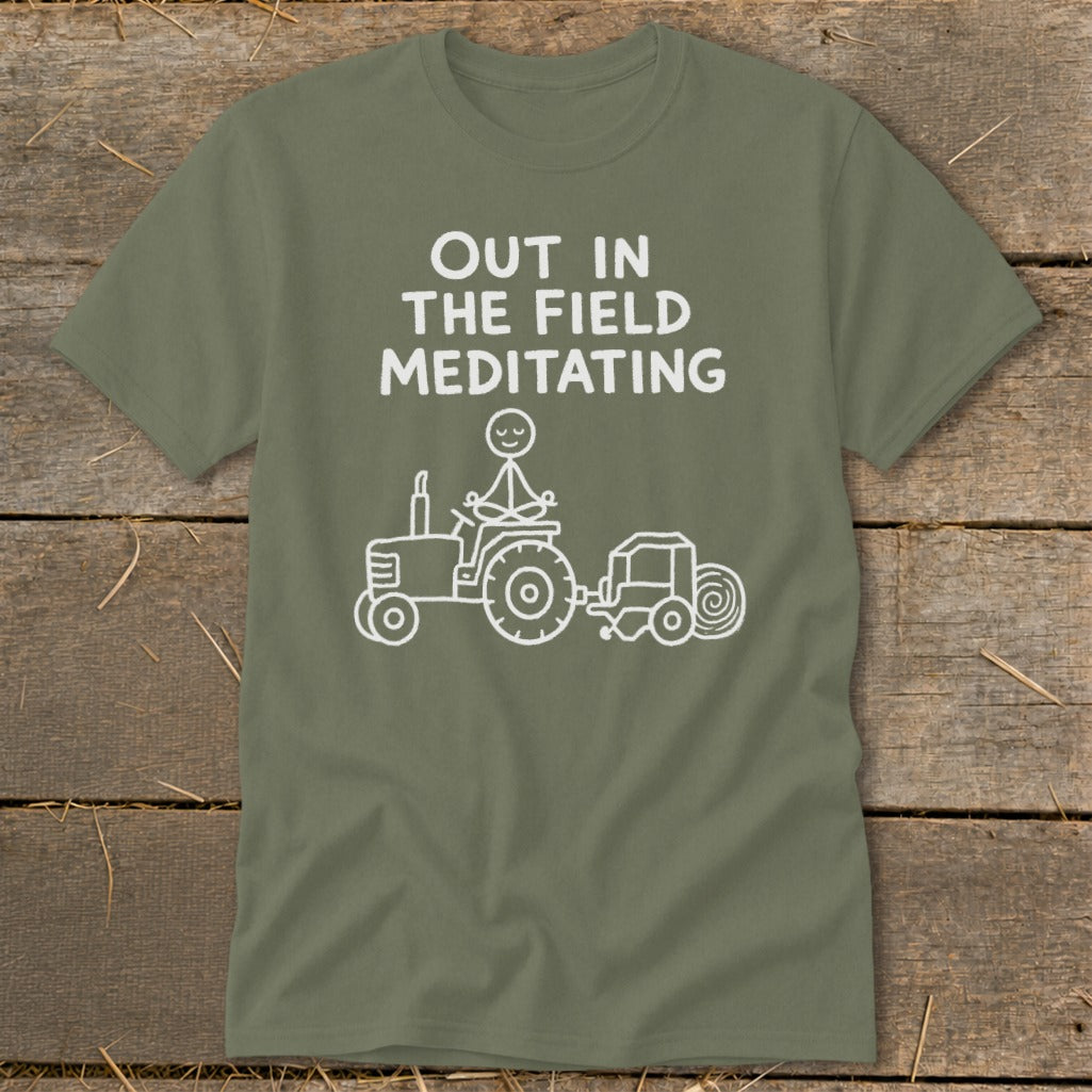Green t-shirt with white text "OUT IN THE FIELD MEDITATING" and a stick figure meditating on a tractor.