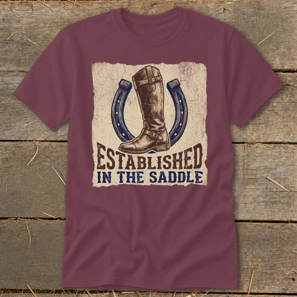 Maroon t-shirt with a graphic of a boot, two horseshoes, and the text "ESTABLISHED IN THE SADDLE".