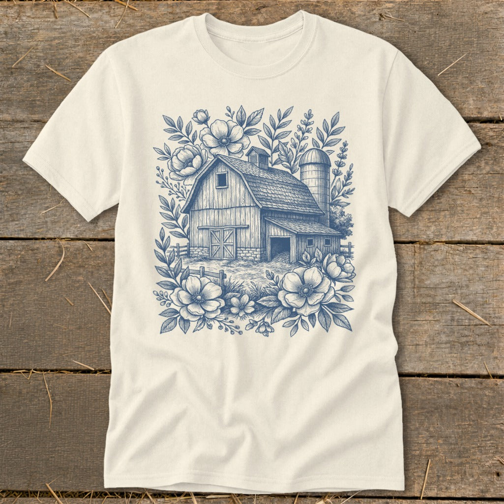 T-shirt with a blue line drawing of a barn surrounded by flowers and foliage.