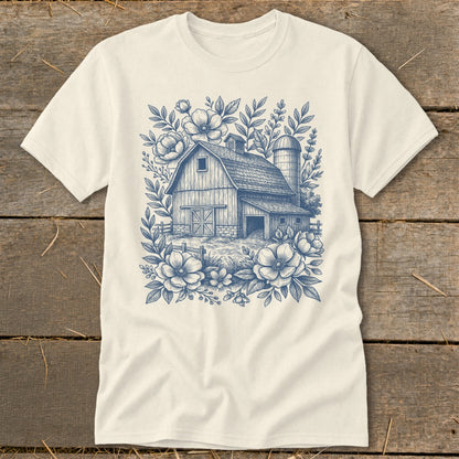T-shirt with a blue line drawing of a barn surrounded by flowers and foliage.