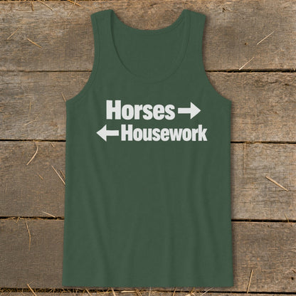 Dark green tank top featuring white text that reads Horses pointing right and Housework pointing left, laid flat on a rustic wooden background.