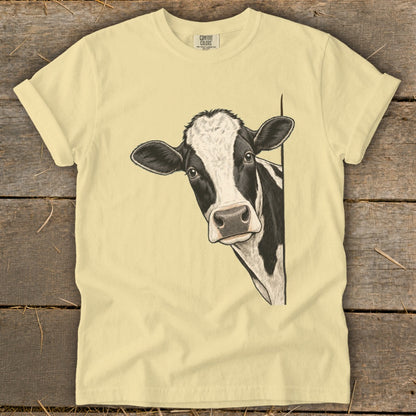 Illustration of a black and white cow peeking around a corner on a pale yellow t-shirt.
