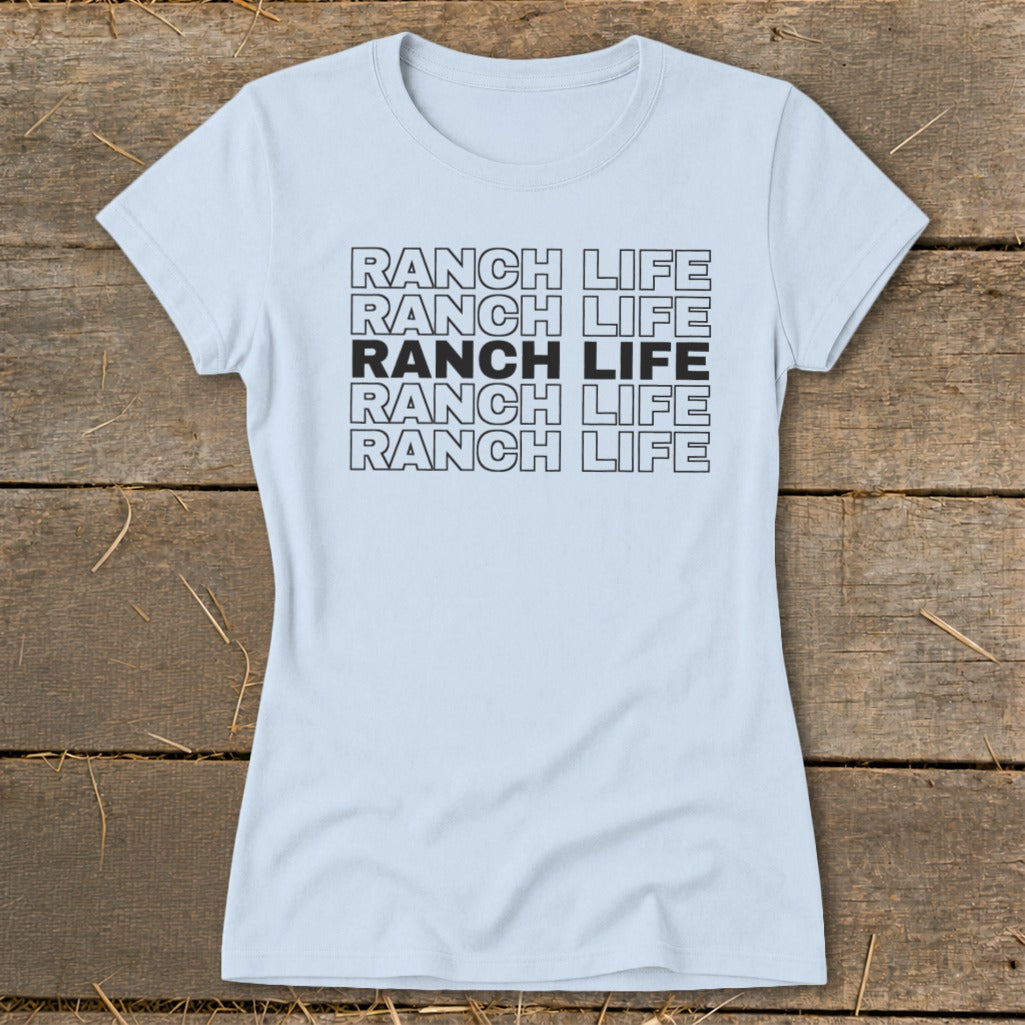 Light blue women's t-shirt printed with stacked black text reading Ranch Life on a wooden background.
