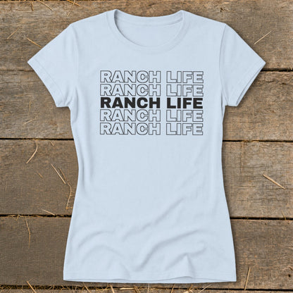 Light blue women's t-shirt printed with stacked black text reading Ranch Life on a wooden background.