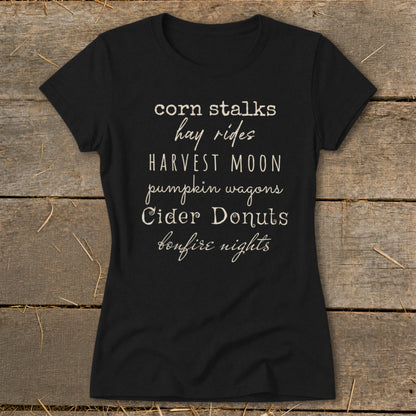 Black t-shirt with white text listing fall activities: corn stalks, hay rides, harvest moon, pumpkin wagons, cider donuts, bonfire nights.