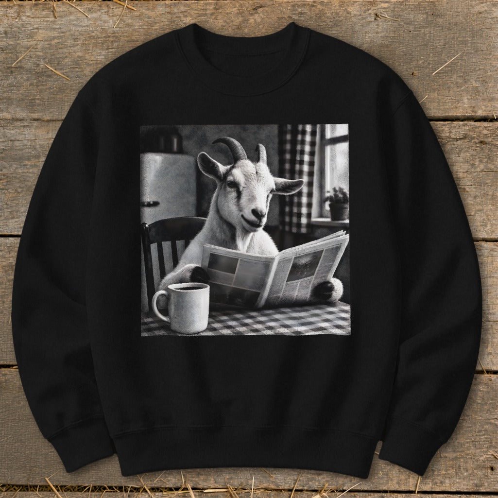 A black crewneck sweatshirt featuring a graphic of a goat sitting at a table, reading a newspaper next to a coffee mug.
