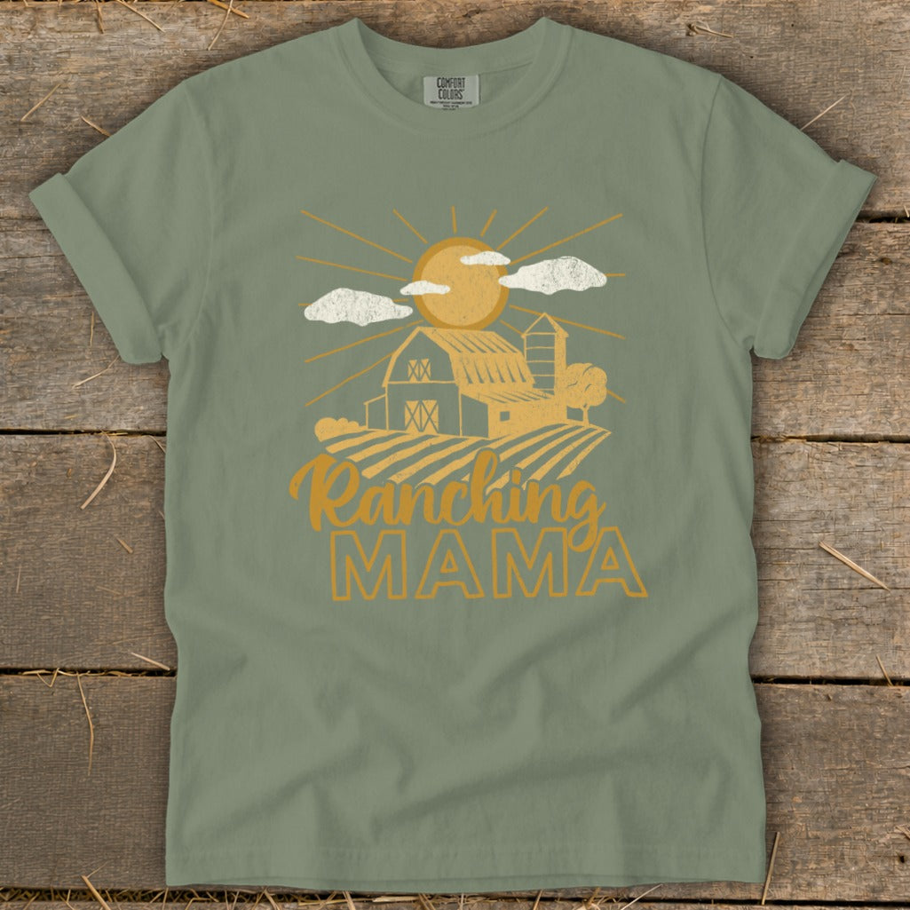 Green t-shirt with a graphic of a barn, sun, clouds, and the text "Ranching MAMA".