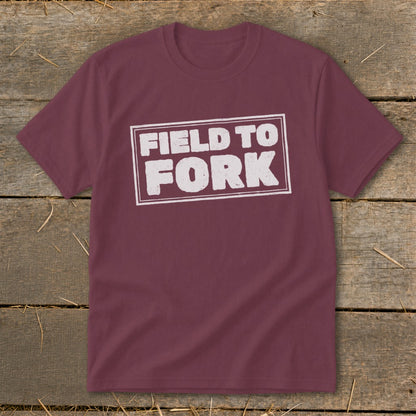 Maroon crewneck t-shirt featuring the distressed white text "Field to Fork" inside a rectangular border, displayed on a rustic wooden background.