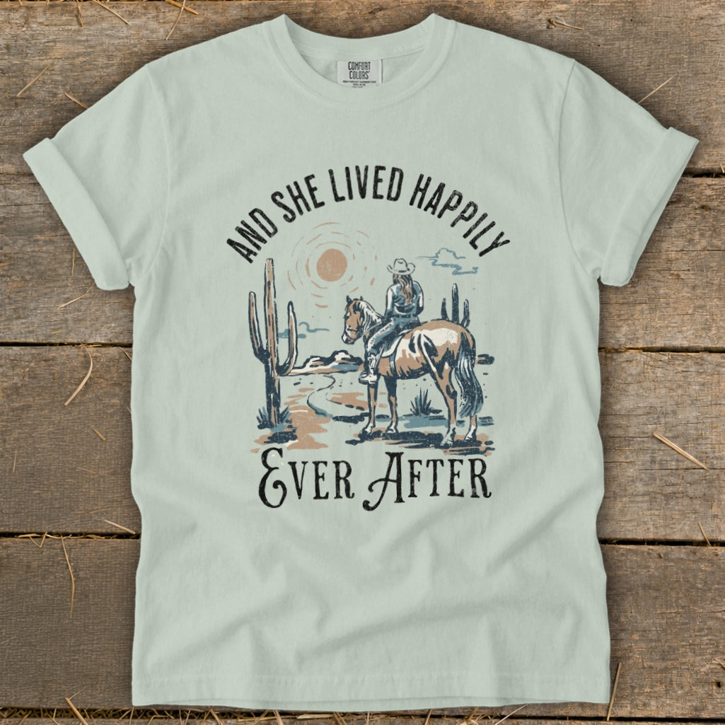 T-shirt graphic of cowgirl on horseback in desert, text "And She Lived Happily Ever After".