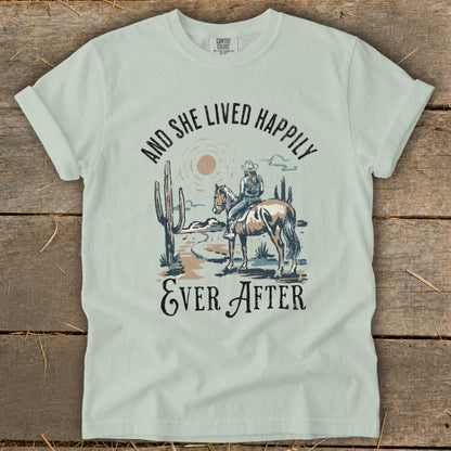 T-shirt graphic of cowgirl on horseback in desert, text "And She Lived Happily Ever After".