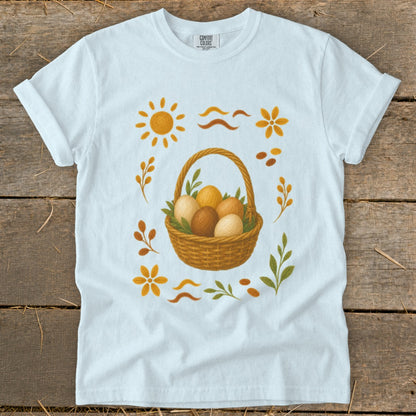 White t-shirt with a woven basket of brown and beige Easter eggs and floral graphics.