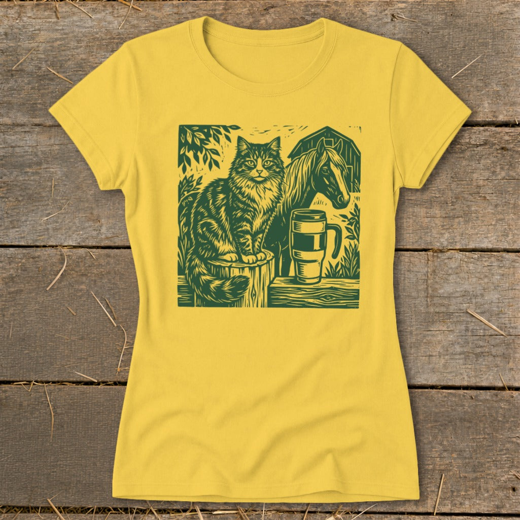 Green linocut print of cat, horse, barn, and mug on a yellow t-shirt.