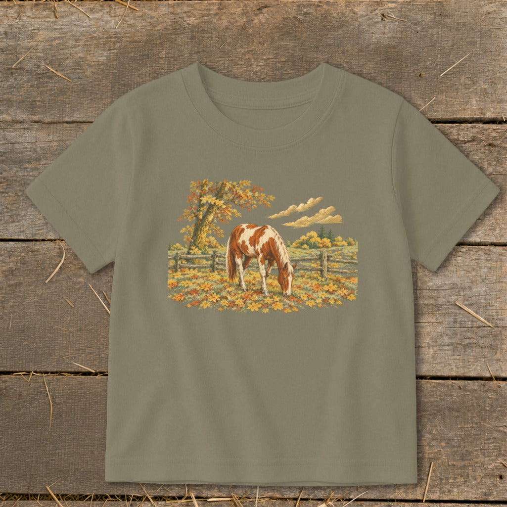 Brown and white horse grazing in a field of fall leaves, under a tree.