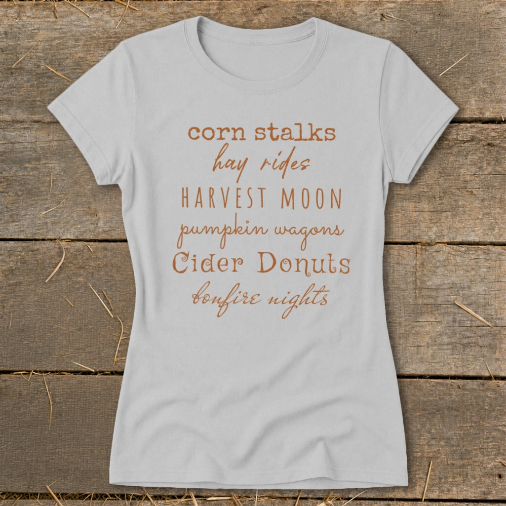 Light grey t-shirt with fall-themed text: corn stalks, hay rides, harvest moon, pumpkin wagons, cider donuts, bonfire nights.