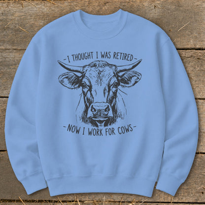 Light blue sweatshirt with cow illustration and text "I thought I was retired - Now I work for cows".