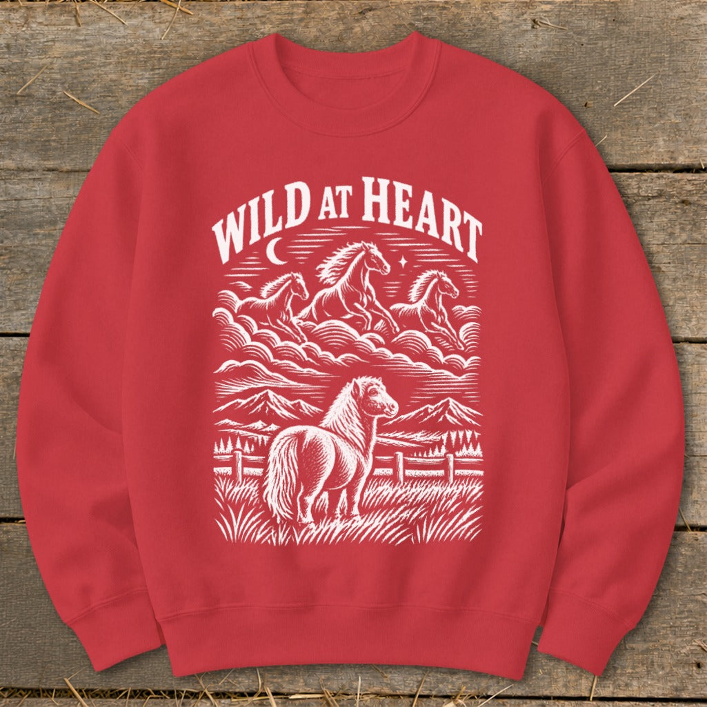 Red sweatshirt with white graphic of horses running and standing in a field with mountains and "WILD AT HEART" text.