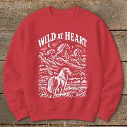 Red sweatshirt with white graphic of horses running and standing in a field with mountains and "WILD AT HEART" text.