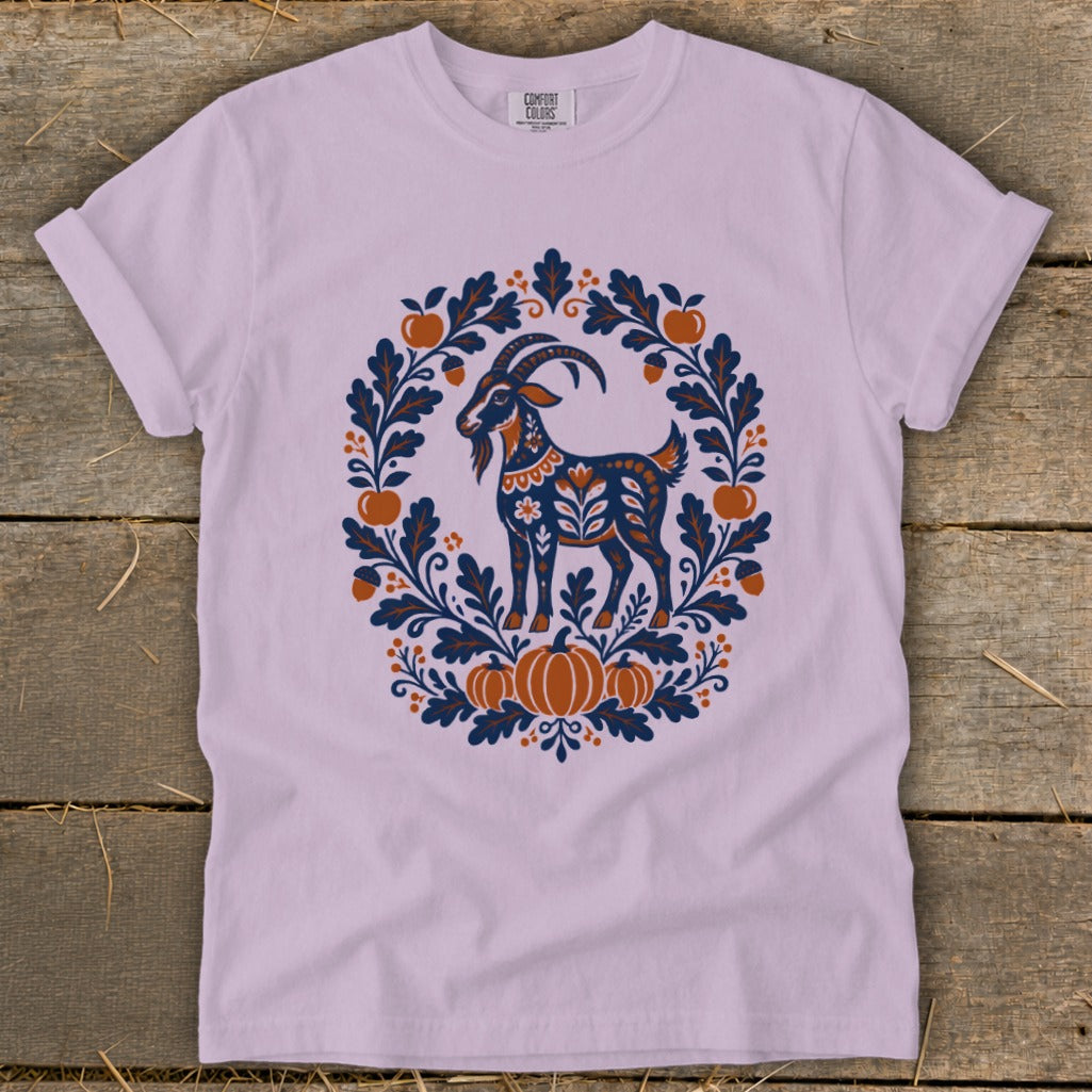Light purple t-shirt featuring a folk art graphic of a goat surrounded by leaves, acorns, apples, and pumpkins.