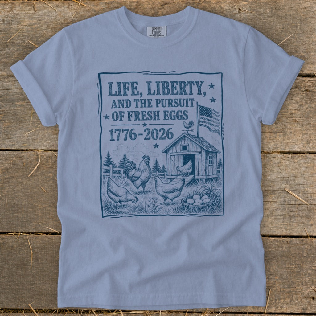 Light blue t-shirt with a graphic of chickens, a coop, and text about the pursuit of fresh eggs.