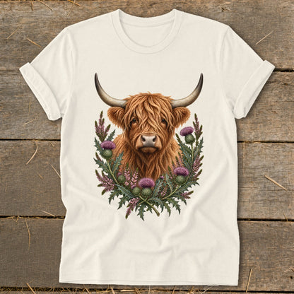 Cream t-shirt with a Highland cow illustration surrounded by thistles.