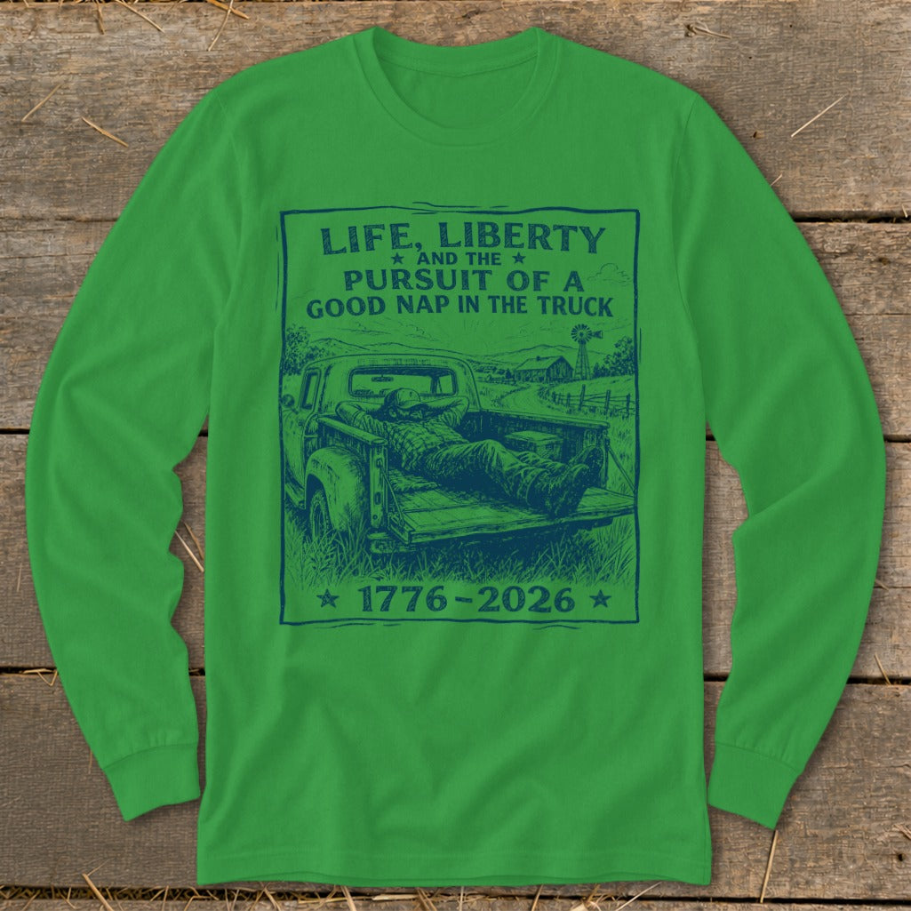 Green long-sleeve shirt with blue graphic of a man napping in a truck, text "Life, Liberty, Pursuit of a Good Nap in the Truck 1776-2026".