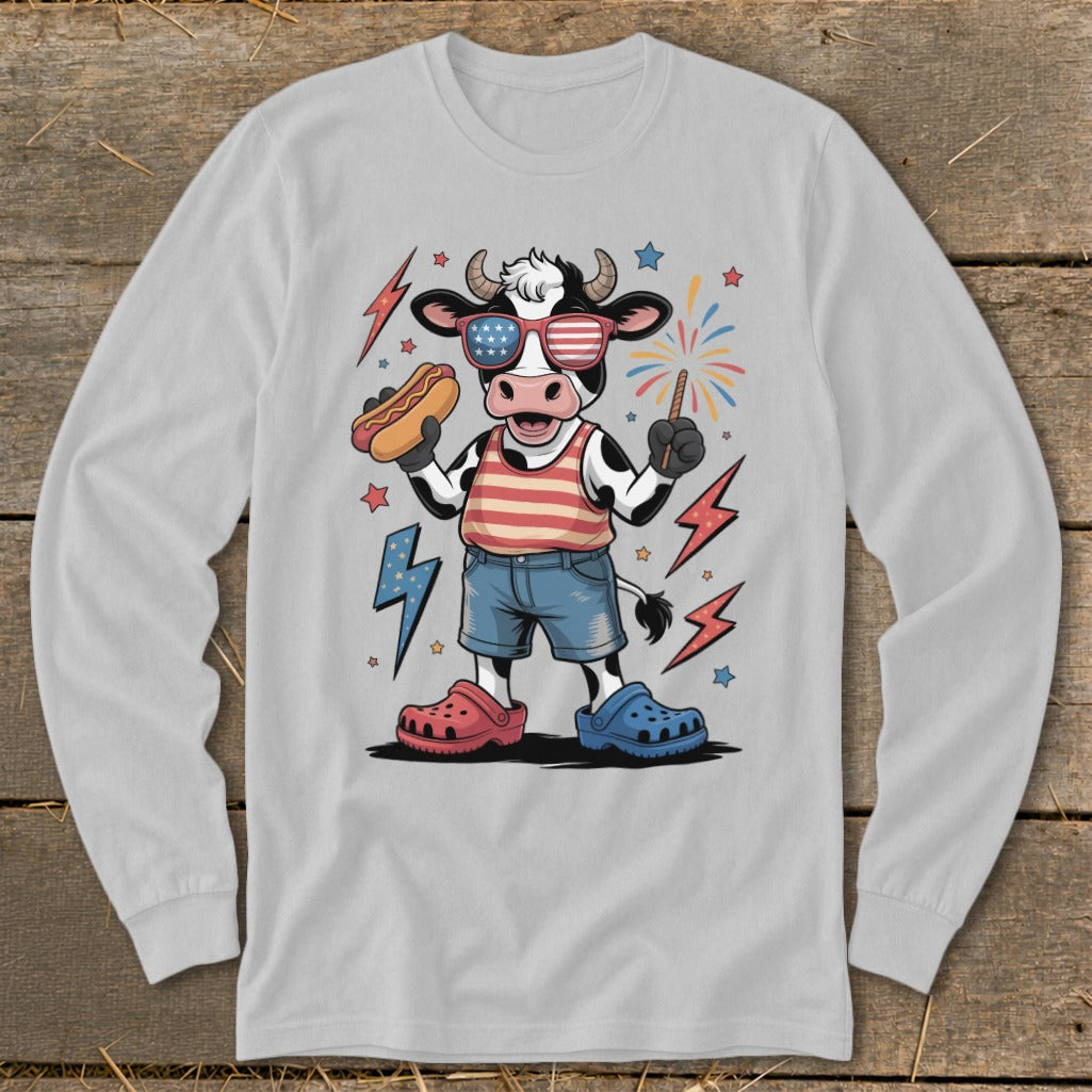 Cow in patriotic sunglasses holding hot dog and sparkler, wearing striped shirt and shorts.