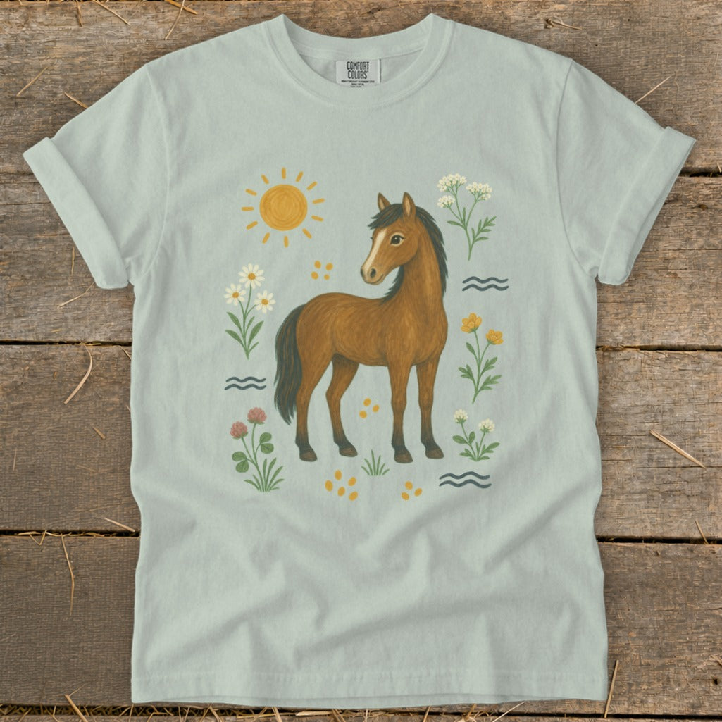Light blue t-shirt with a brown horse illustration surrounded by sun, flowers, and water waves.