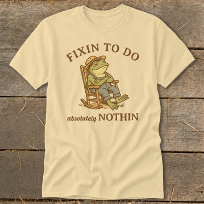 Cream t-shirt with cartoon frog in rocking chair reading "Fixin to do absolutely nothin".