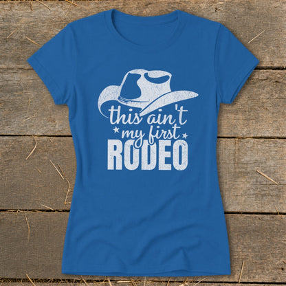 Blue t-shirt with white text and cowboy hat graphic reading "this ain't my first RODEO".