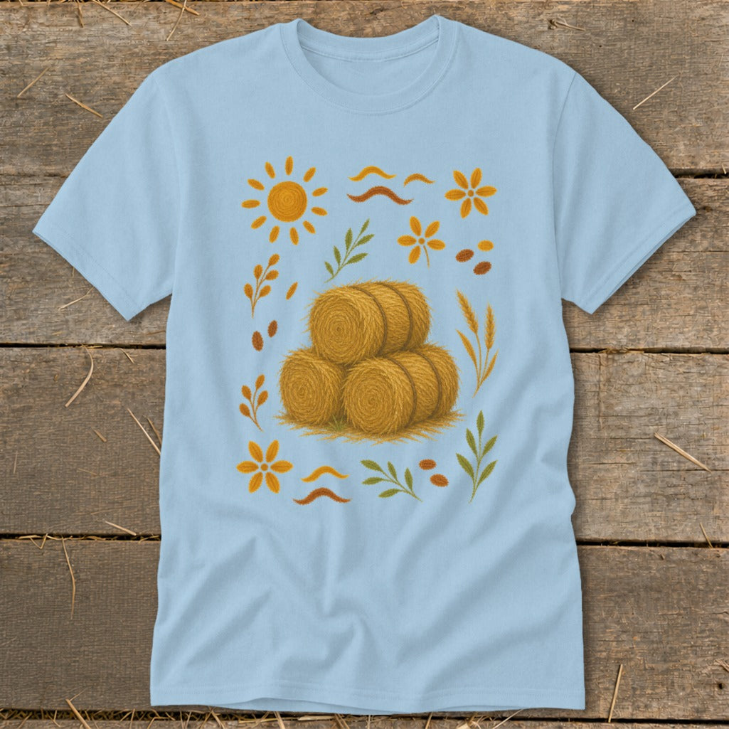 Light blue t-shirt with stacked hay bales and autumn foliage illustration.