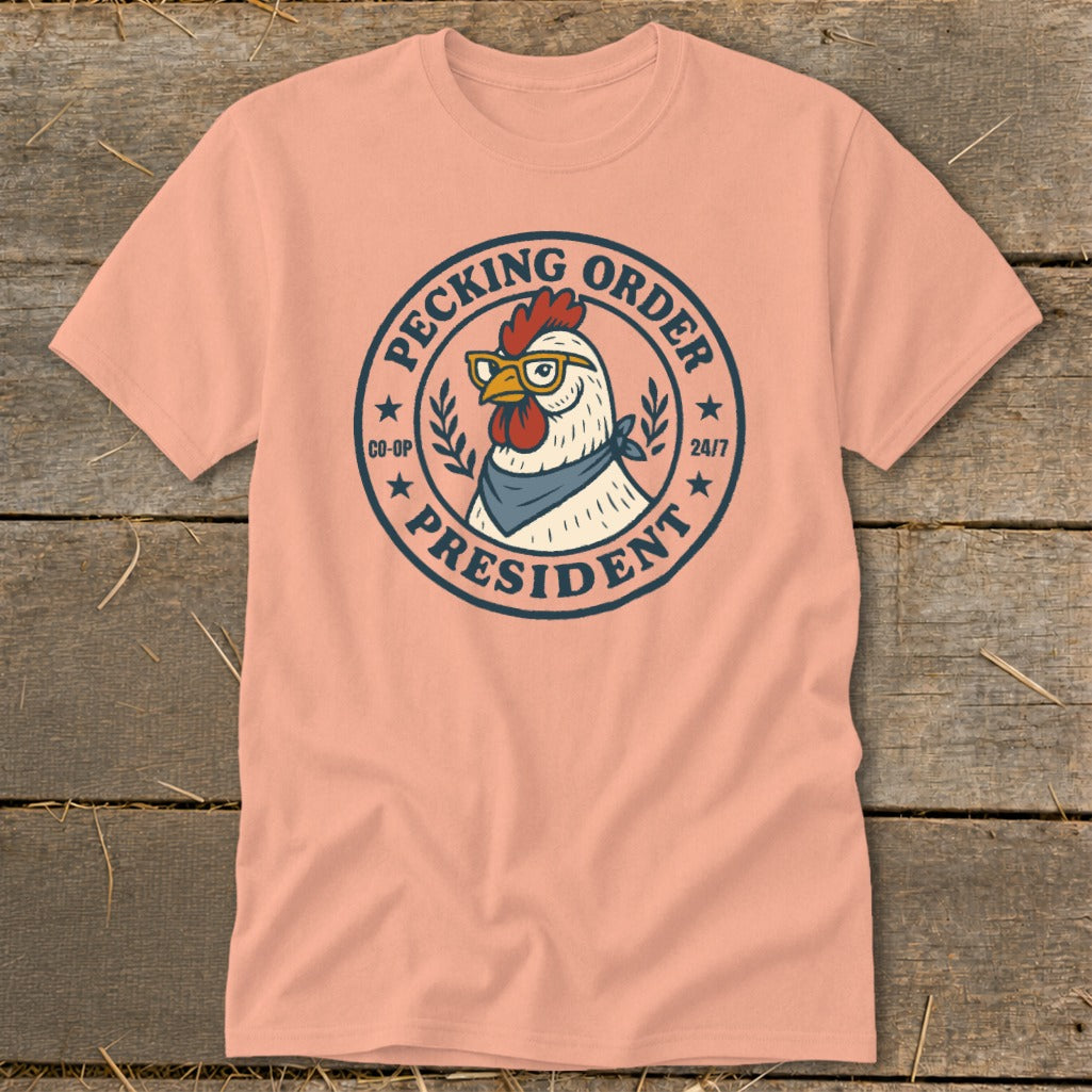 Peach t-shirt with a round graphic of a chicken wearing glasses and bandana, labeled "Pecking Order President".