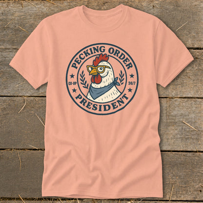 Peach t-shirt with a round graphic of a chicken wearing glasses and bandana, labeled "Pecking Order President".