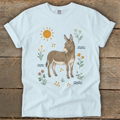 Light blue t-shirt with a donkey illustration surrounded by flowers and sun.
