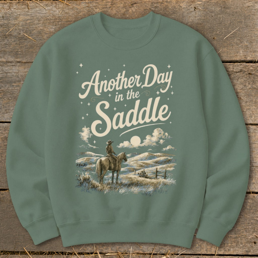 Green sweatshirt with "Another Day in the Saddle" text and cowboy on horseback graphic.