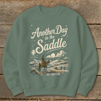 Green sweatshirt with "Another Day in the Saddle" text and cowboy on horseback graphic.