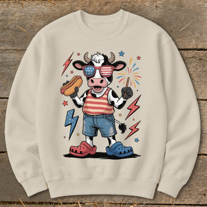 Cow wearing patriotic sunglasses holding a hot dog and sparkler, surrounded by lightning bolts and fireworks.