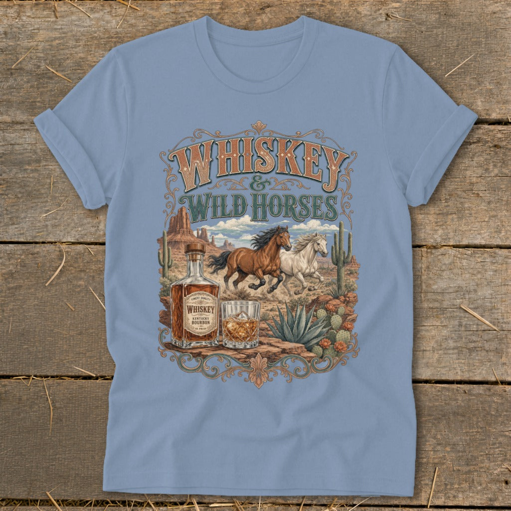 Light blue t-shirt graphic: Whiskey and Wild Horses in desert landscape with bottle and glass.