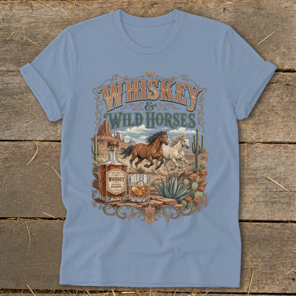 Light blue t-shirt graphic: Whiskey and Wild Horses in desert landscape with bottle and glass.