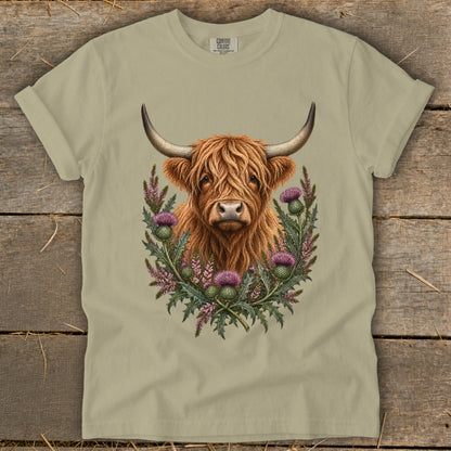 Highland cow surrounded by thistles and heather on a tan t-shirt.
