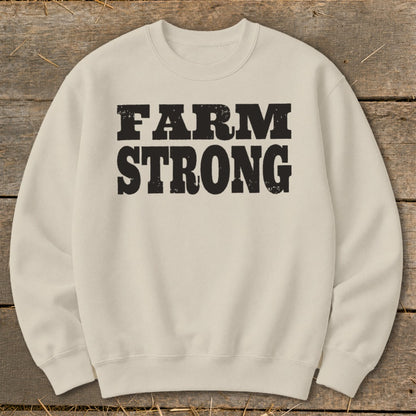 Beige crewneck sweatshirt with distressed black text on the chest reading FARM STRONG laid flat on rustic wood.