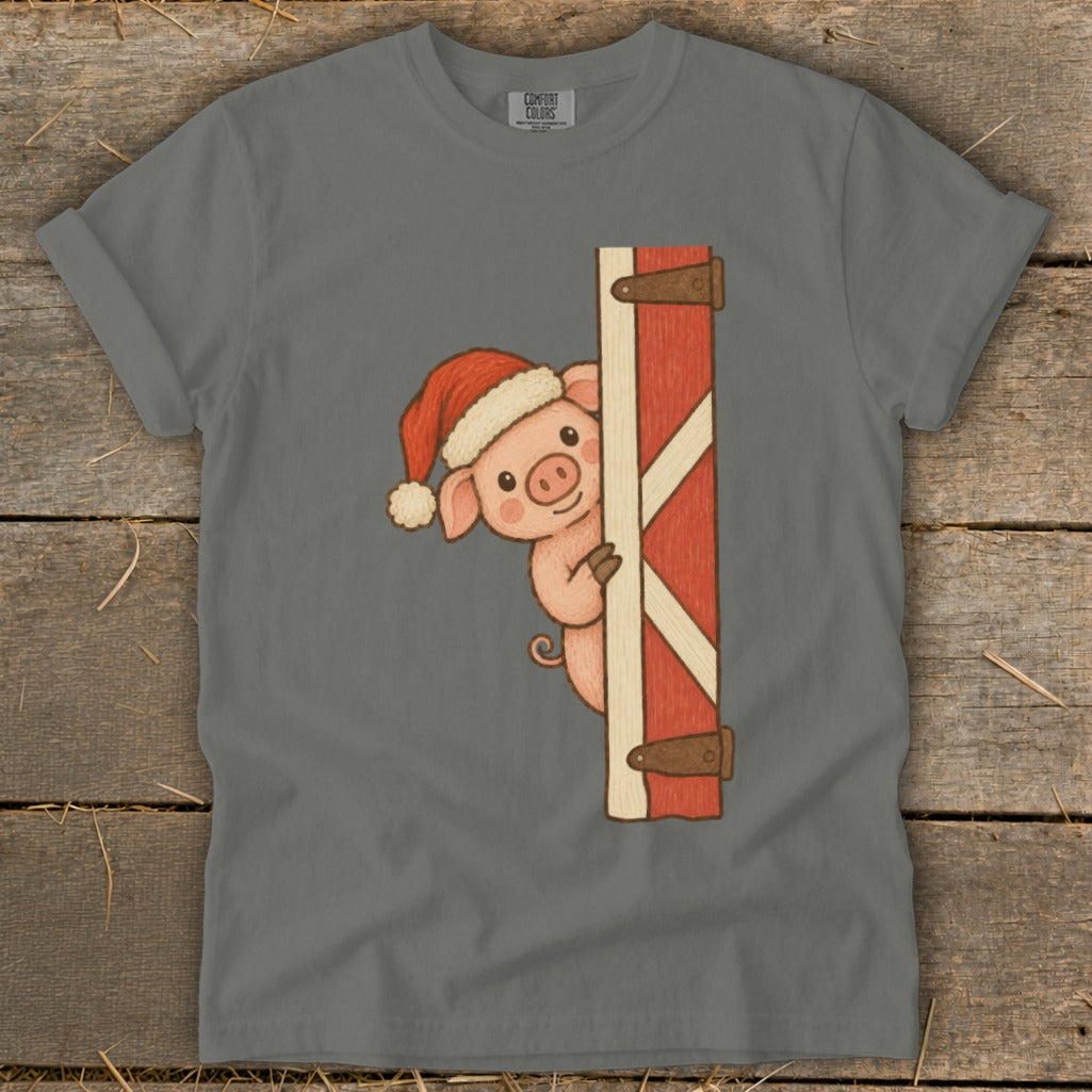 Pig wearing Santa hat peeks from behind a red barn door on a gray t-shirt.