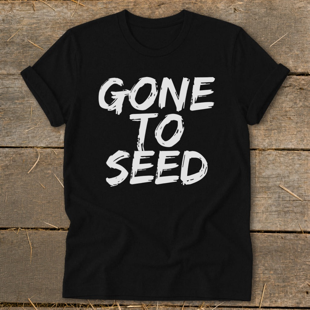 Black t-shirt with white text reading "GONE TO SEED" on a wooden background.