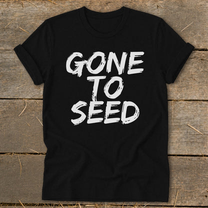Black t-shirt with white text reading "GONE TO SEED" on a wooden background.
