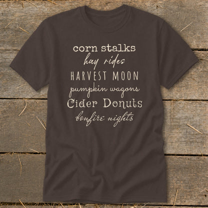 Brown t-shirt with white text listing fall activities: corn stalks, hay rides, harvest moon, pumpkin wagons, cider donuts, bonfire nights.