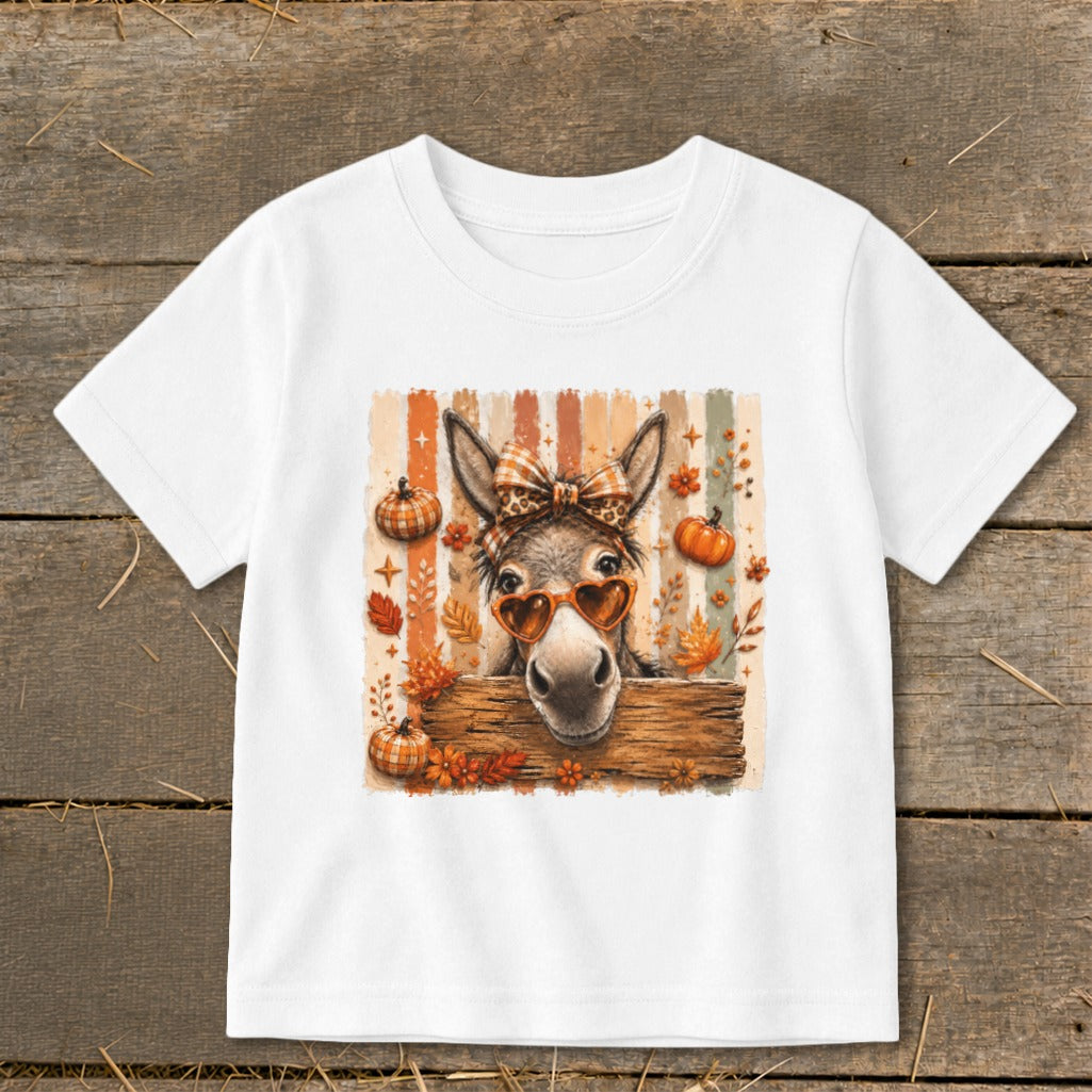Donkey with heart sunglasses and bow peeking over wooden sign with pumpkins and leaves.