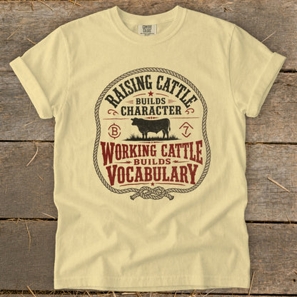 Light yellow t-shirt with "Raising Cattle Builds Character, Working Cattle Builds Vocabulary" graphic.